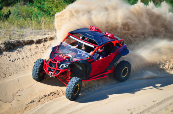 A red dune buggy speeds through sandy terrain, kicking up a large cloud of dust. The scene is dynamic and adventurous, conveying excitement and action.